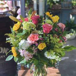 Mixed bouquet of roses, lilies, sunflowers, and hydrangeas in a glass vase