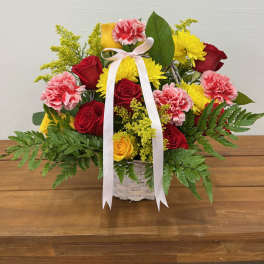 Basket arrangement of red and yellow roses with pink carnations and a white ribbon