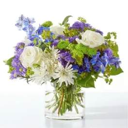 Bouquet of white roses, blue and purple flowers in a clear glass vase