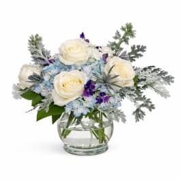 White roses and blue flowers in a clear glass vase