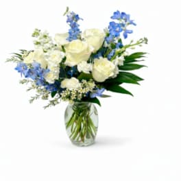 White roses and blue flowers arranged in a clear glass vase