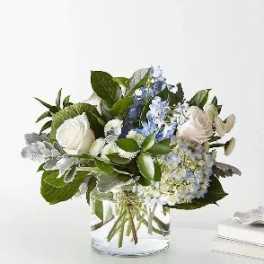 Short arrangement of white roses and blue hydrangeas in a clear glass cylinder vase