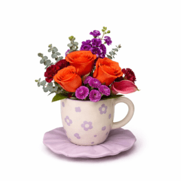 Compact orange and purple flower arrangement in a patterned mug on a lilac saucer
