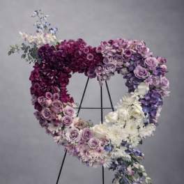 Heart-shaped floral wreath on a black stand with purple, pink, and white blooms