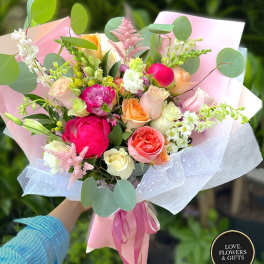 Hand-tied bouquet of pink peonies and mixed roses wrapped in pink paper with ribbon