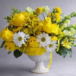 Yellow and white floral arrangement in a white pedestal vase