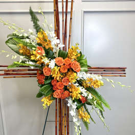 Tall cross-shaped bamboo standing spray with orange roses, yellow and white orchids, and tropical foliage.