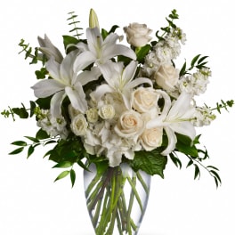 White lilies, roses, hydrangeas, and stock arranged in a clear glass vase