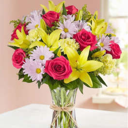 Bouquet of pink roses, yellow lilies, and pale daisies in a glass vase