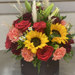 Bouquet of sunflowers, red roses, and pink carnations in a dark box vase