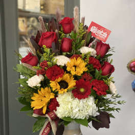 Mixed bouquet of red roses, yellow sunflowers, and white hydrangea in a decorative vase