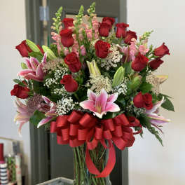 Bouquet of red roses and pink lilies in a glass vase with a red ribbon