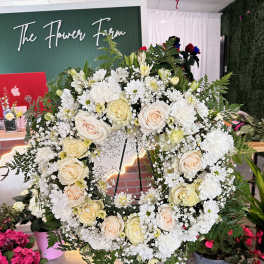 Large white floral wreath on a stand with cream roses and daisies