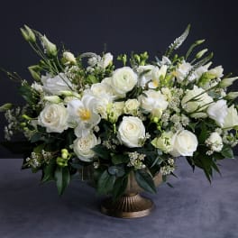 Large white floral arrangement in a bronze pedestal vase