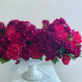 Deep pink and burgundy flower arrangement in a white pedestal vase