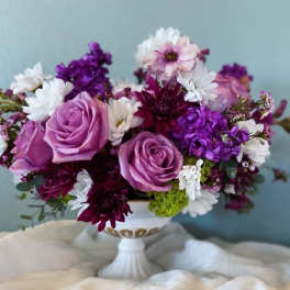 Purple and white floral arrangement in a white pedestal vase