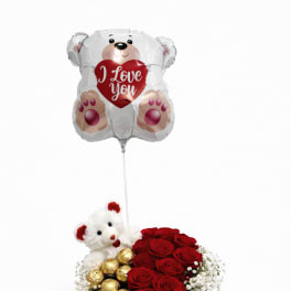 Red roses with a teddy bear, chocolates, and a heart balloon in a gift box