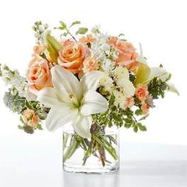 Peach roses and white lilies in a clear glass vase