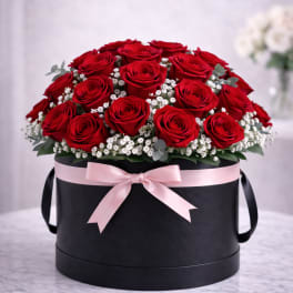 Red roses arranged in a black round box with a pink ribbon