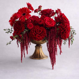 Red roses and gerbera daisies arranged in a gold pedestal vase
