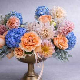 Bouquet of blue, peach, and blush flowers in a gold pedestal vase