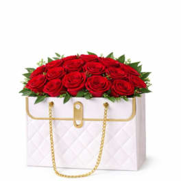 Red roses arranged in a white quilted handbag-style box with gold chain handles.
