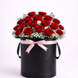 Red roses arranged in a black hatbox with a pink ribbon