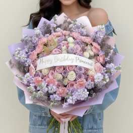 Large pastel bouquet of roses, carnations, and lilac flowers with a birthday ribbon