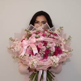Woman holding a large pink bouquet of roses with a ribbon bow