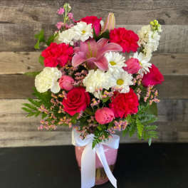 Mixed bouquet of pink, red, and white flowers in a pink vase with a white ribbon