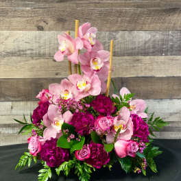 Pink orchids and roses arranged with magenta blooms in a low bouquet