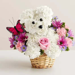 White teddy bear floral arrangement in a wicker basket with pink and purple flowers