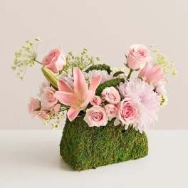Pink roses and lilies arranged in a moss-covered rectangular container