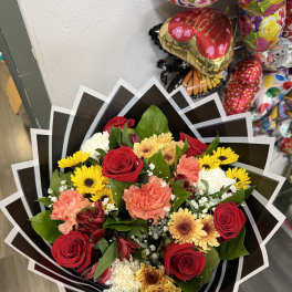 Mixed bouquet of red roses, yellow daisies, and carnations in black wrap