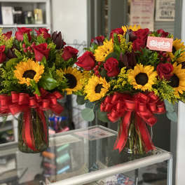 Two bouquets of red roses and sunflowers in glass vases with red bows