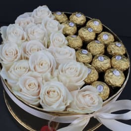White roses and gold-wrapped chocolates in a round gift box with a ribbon