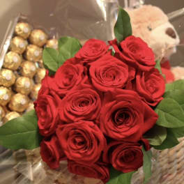 Bouquet of red roses with green leaves beside chocolates and a teddy bear