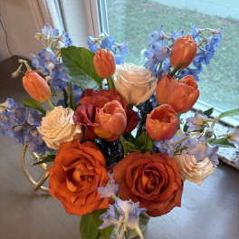 Bouquet of orange roses, cream roses, and blue flowers in a vase