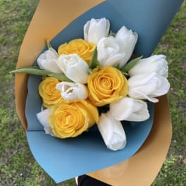 Bouquet of yellow roses and white tulips wrapped in blue and tan paper