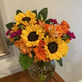 Bouquet of sunflowers, orange roses, and magenta flowers in a glass vase