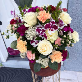 Mixed bouquet of cream roses, orchids, and carnations in a vase