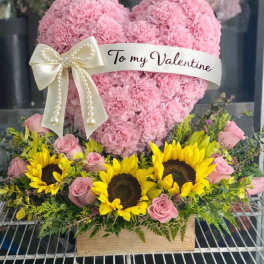 Pink heart-shaped floral arrangement with a Valentine ribbon and sunflowers below