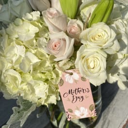 White roses and pale hydrangeas with green lily buds in a glass vase