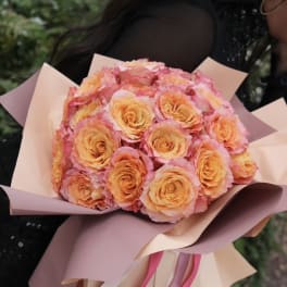 Bouquet of peach and pink roses wrapped in blush paper with ribbons