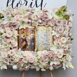 Large floral wreath with pale roses and white lilies around a central religious icon