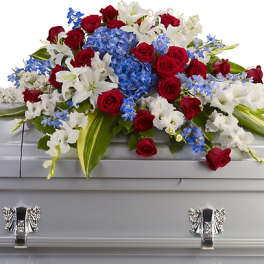 Red roses, white lilies, and blue flowers arranged on a silver casket
