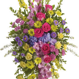Standing floral spray with pink roses and purple flowers on a white easel
