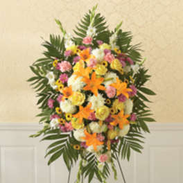 Standing floral spray with orange lilies, pink and white flowers, and palm leaves