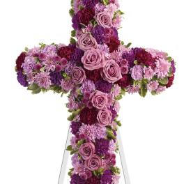 Cross-shaped floral tribute in pink, purple, and burgundy flowers on a white easel