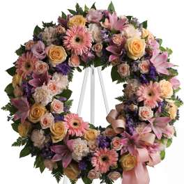 Pink and peach floral wreath on a white easel with a ribbon bow